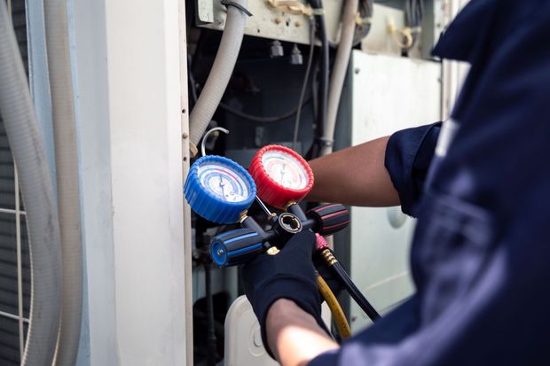 HVAC technician in blue uniform checks air conditioning unit pressure with gauges.