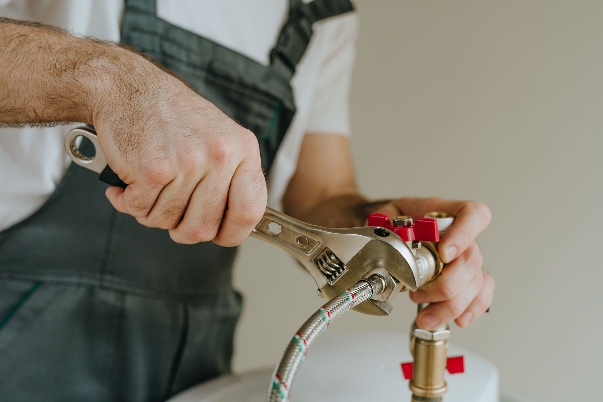 Plumber tightening a pipe with a wrench, wearing grey overalls.