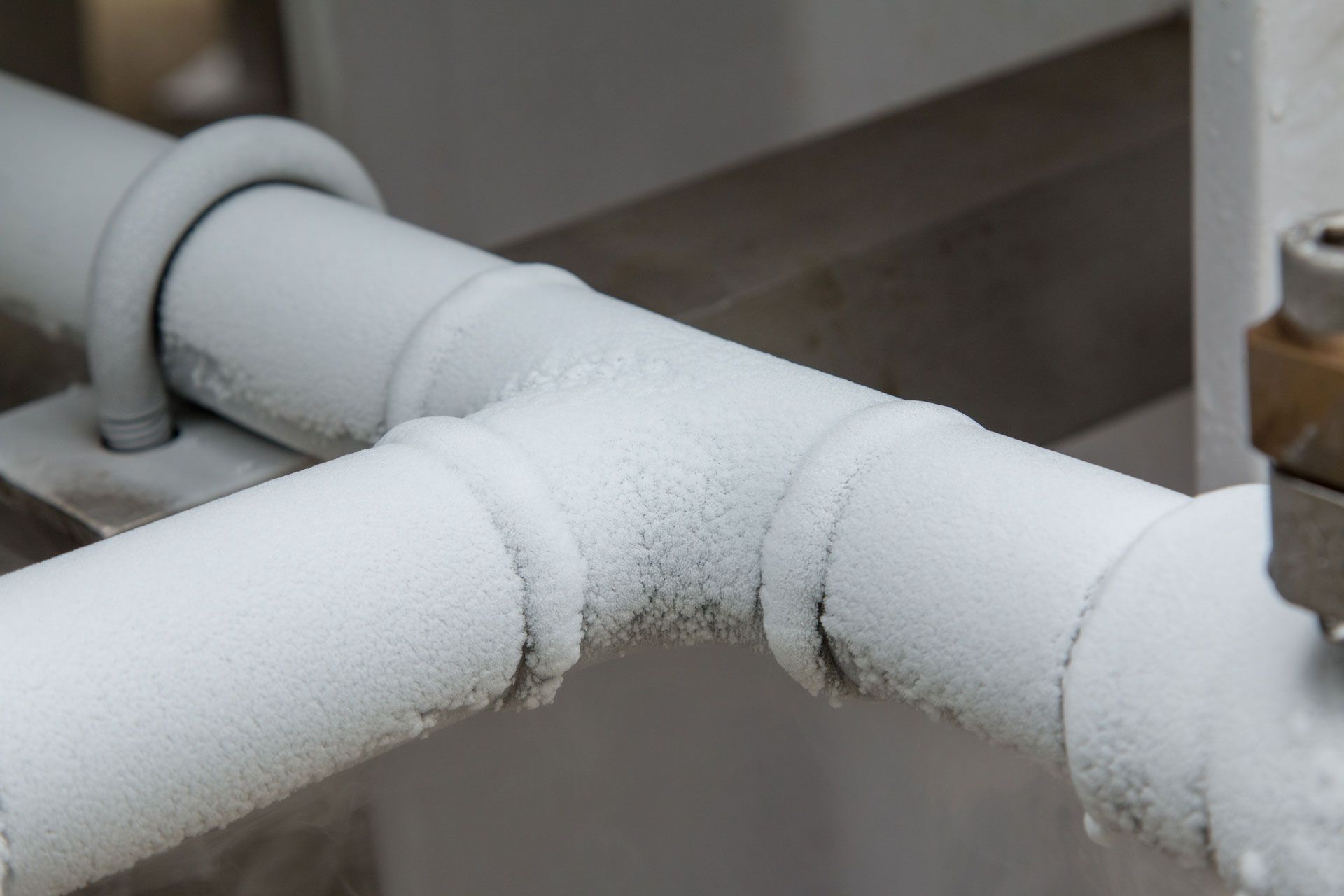 Frost-covered pipes and fittings, likely a refrigeration system, in a close-up view.