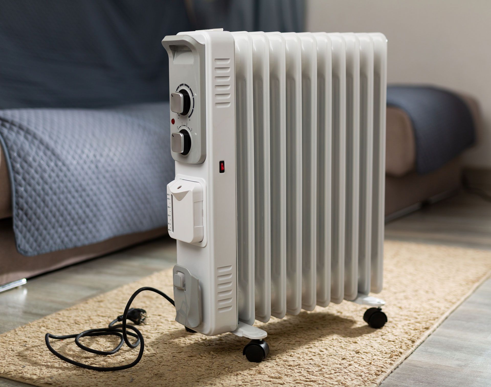 Oil-filled radiator heater on a rug, near a couch. White with black controls.