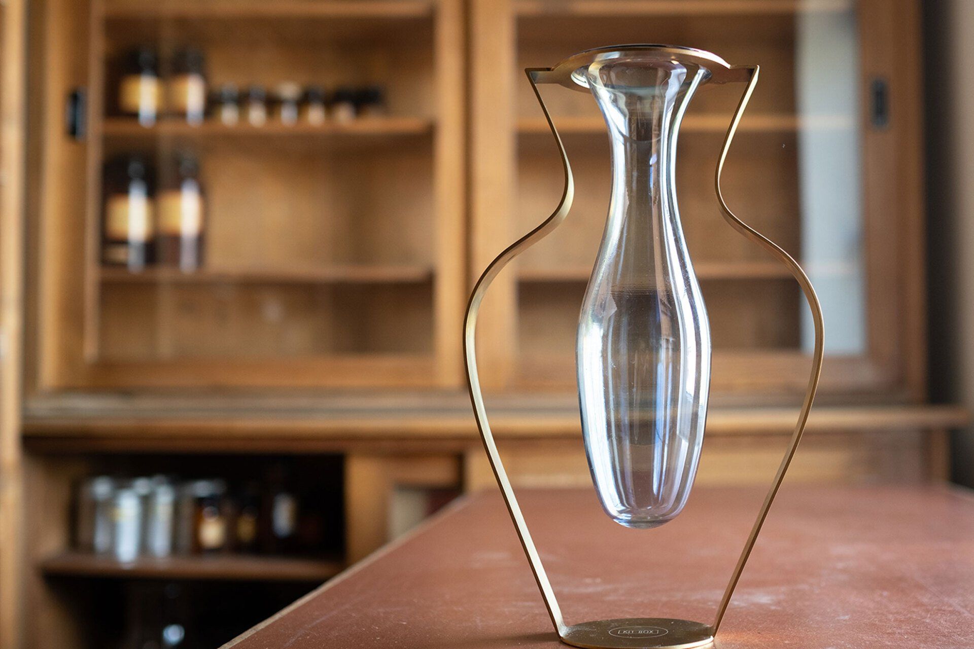 Eine Glasvase steht auf einem Tisch vor einem Holzschrank.