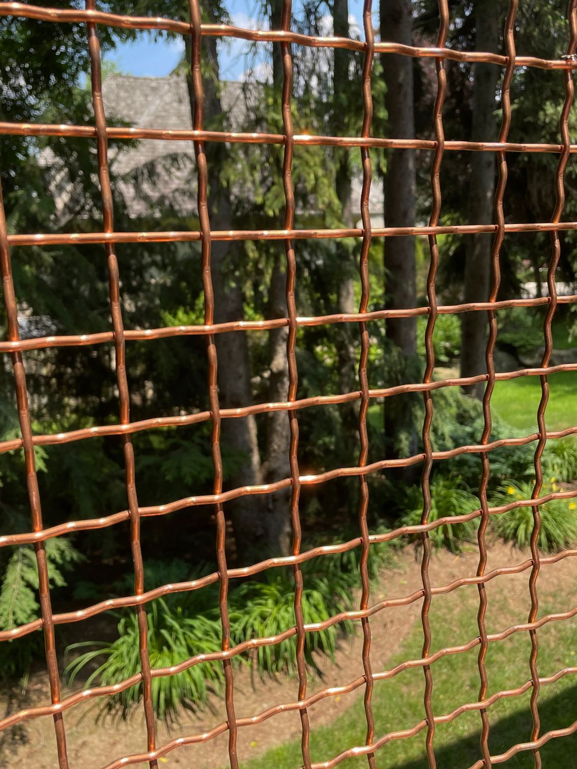 A close up of a copper wire fence with trees in the background