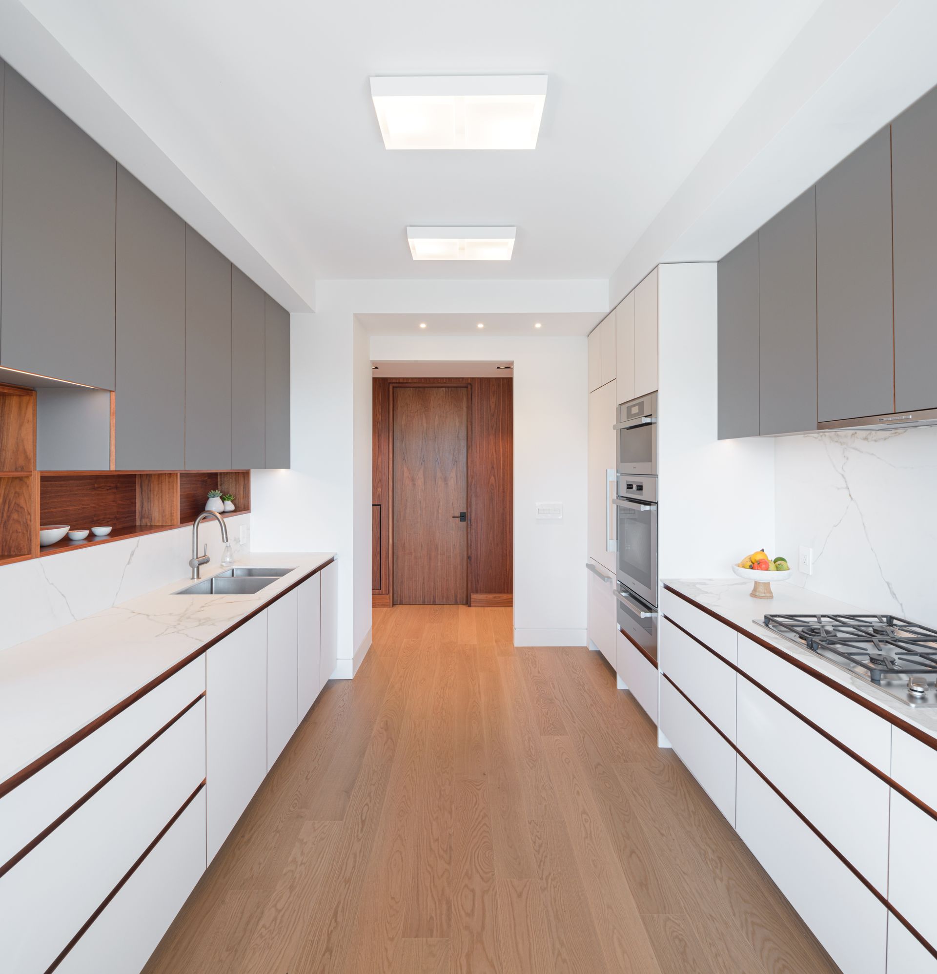 A long kitchen with white cabinets and wooden floors