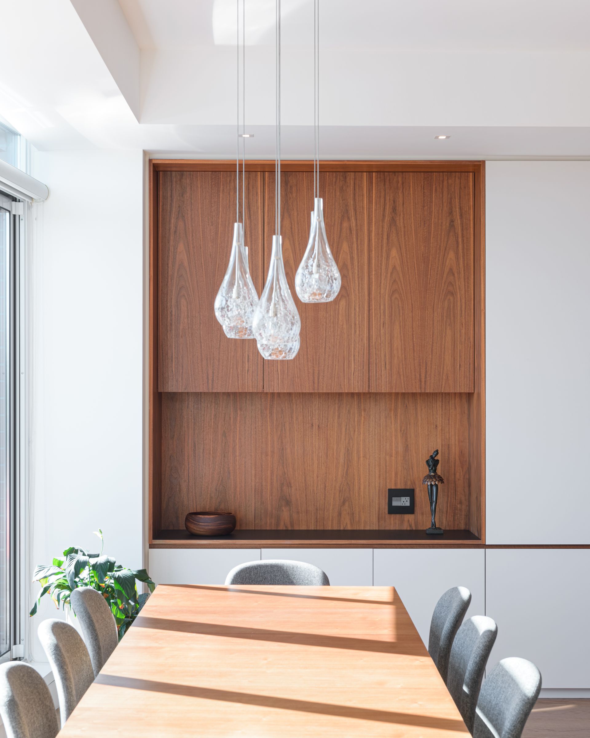 A dining room with a wooden table and chairs and three pendant lights hanging from the ceiling.