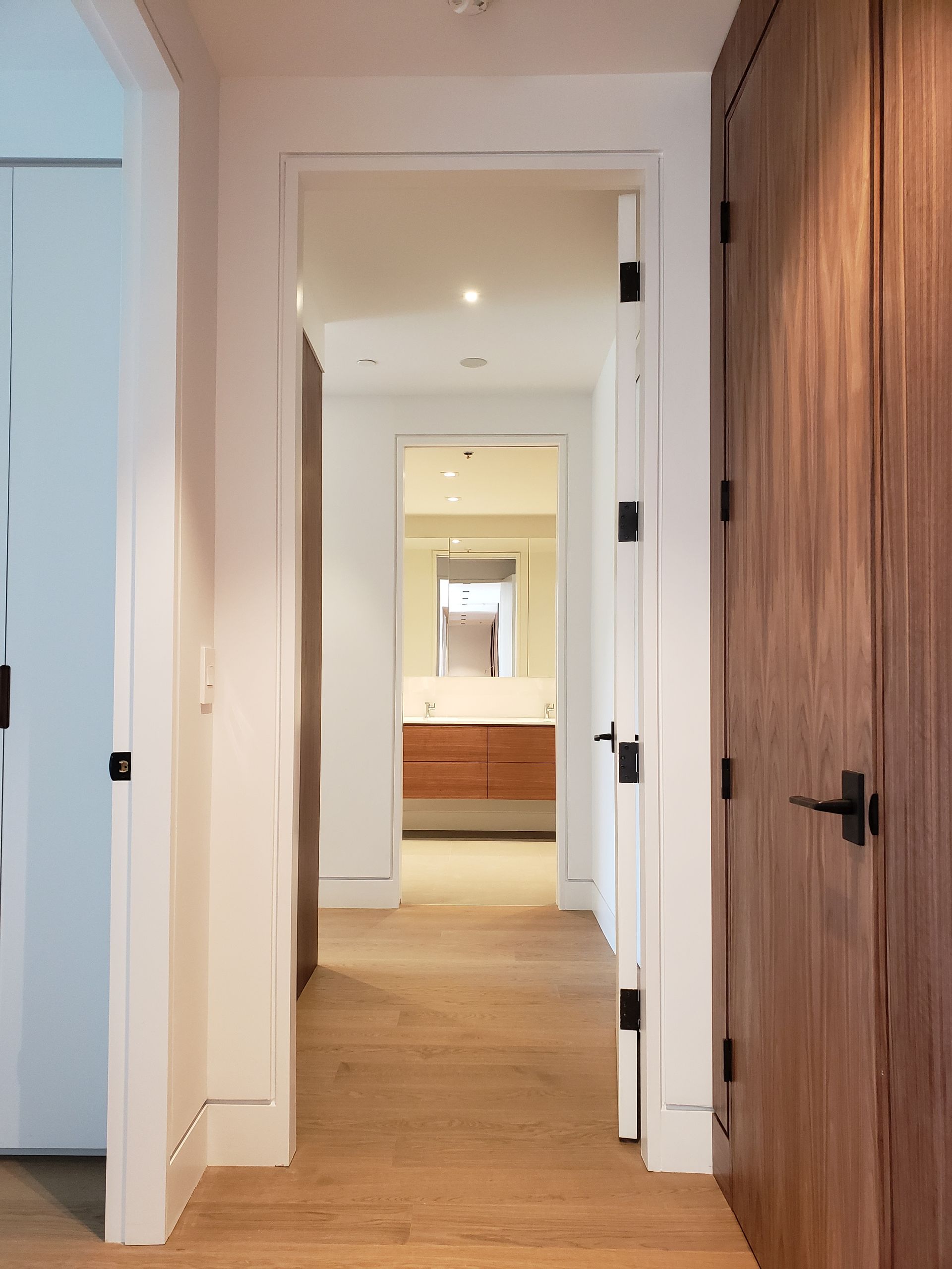A hallway with a wooden floor and a wooden door leading to a bathroom.