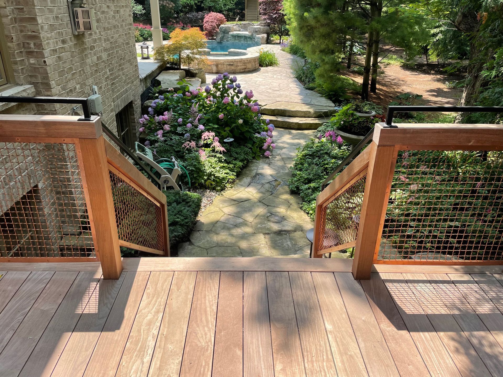 A wooden deck with stairs leading up to a garden and a pool.