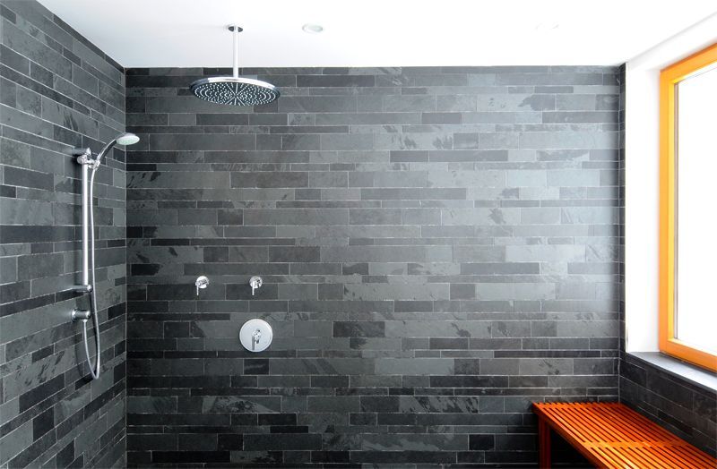 A bathroom with black tiles and a shower head