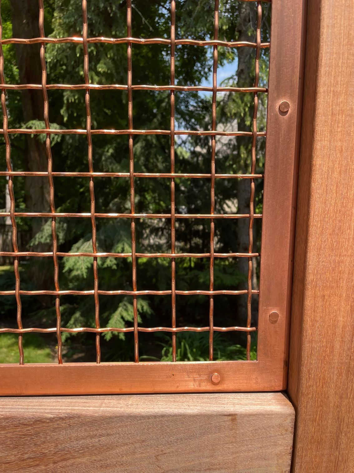 A close up of a copper fence with trees in the background