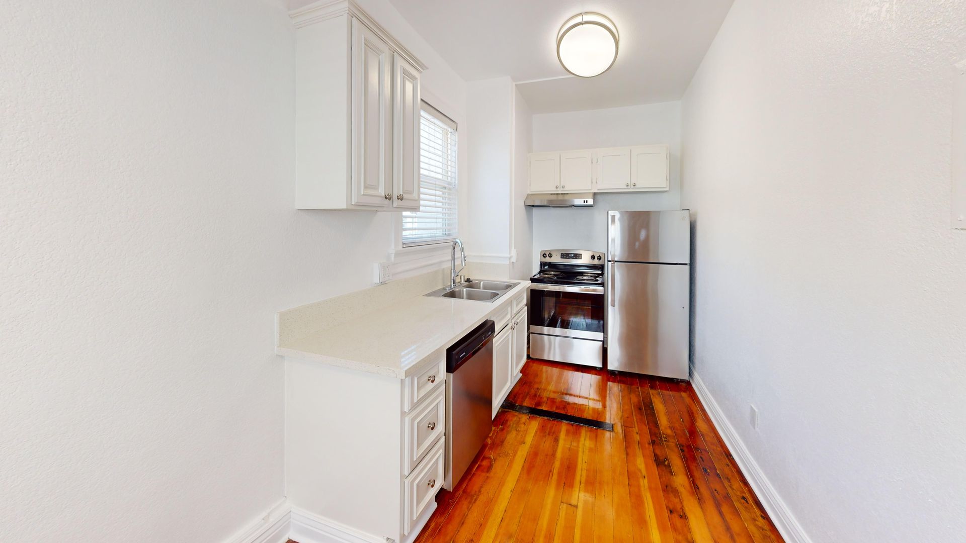 Small, white kitchen with stainless steel appliances, hardwood floor, and white cabinets.