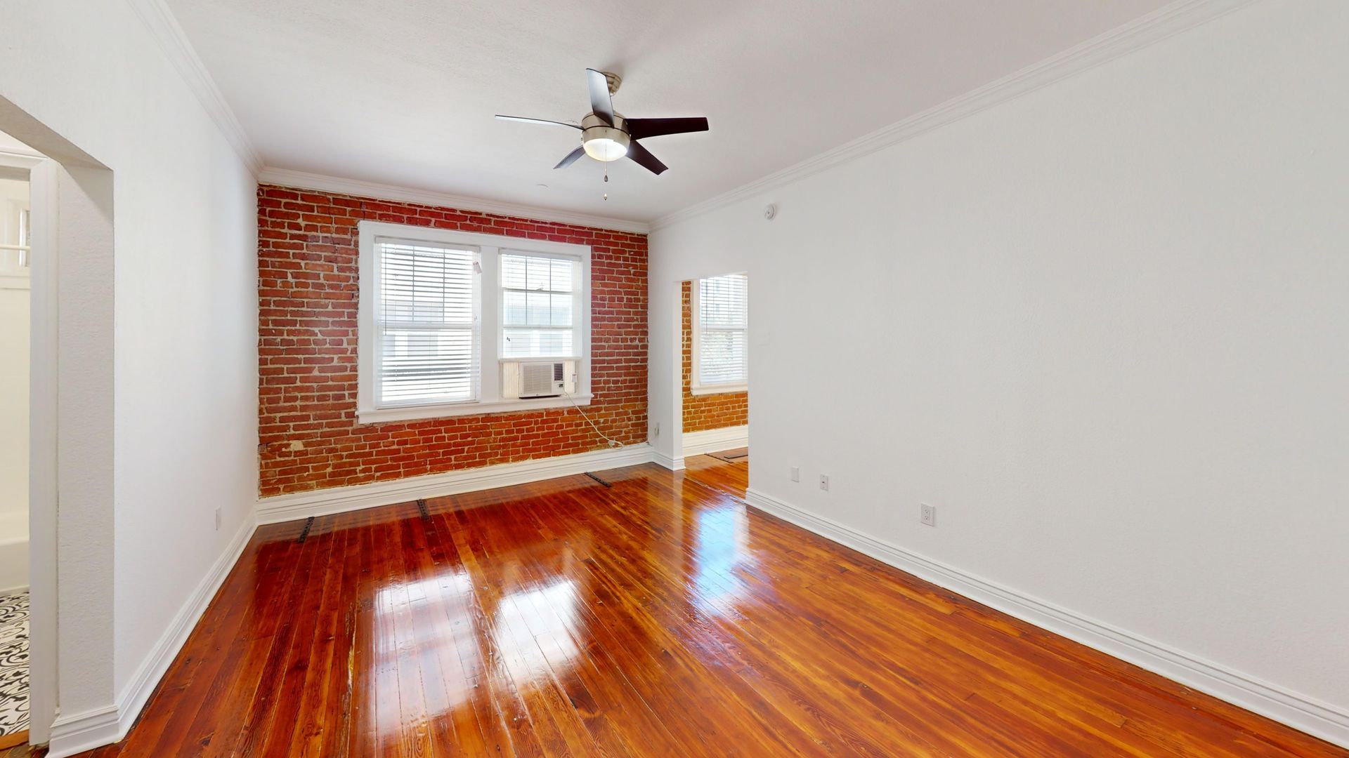 Interior room with exposed brick wall, hardwood floors, and a ceiling fan.