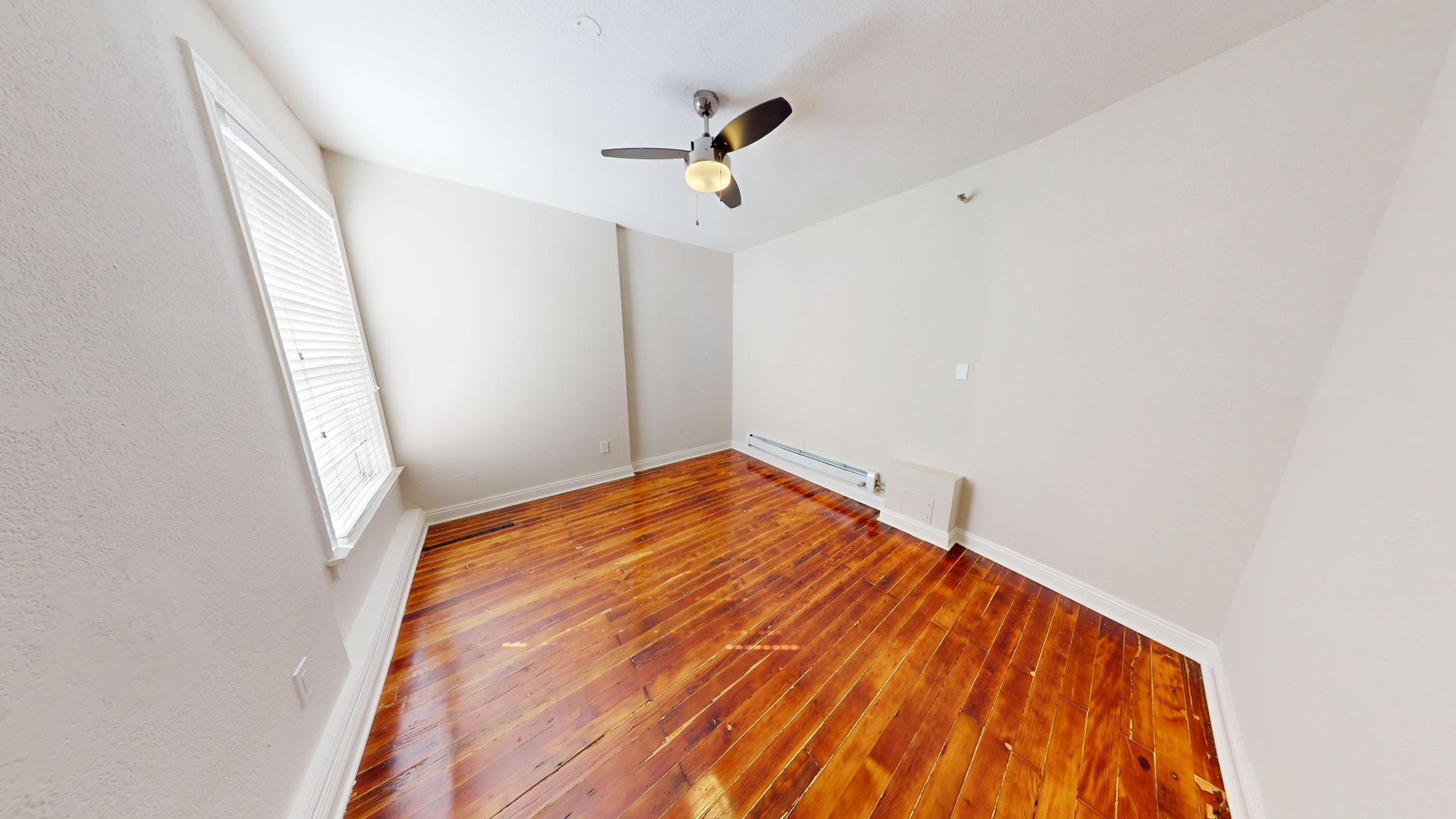 Empty room with hardwood floors, a ceiling fan, and a window with blinds.