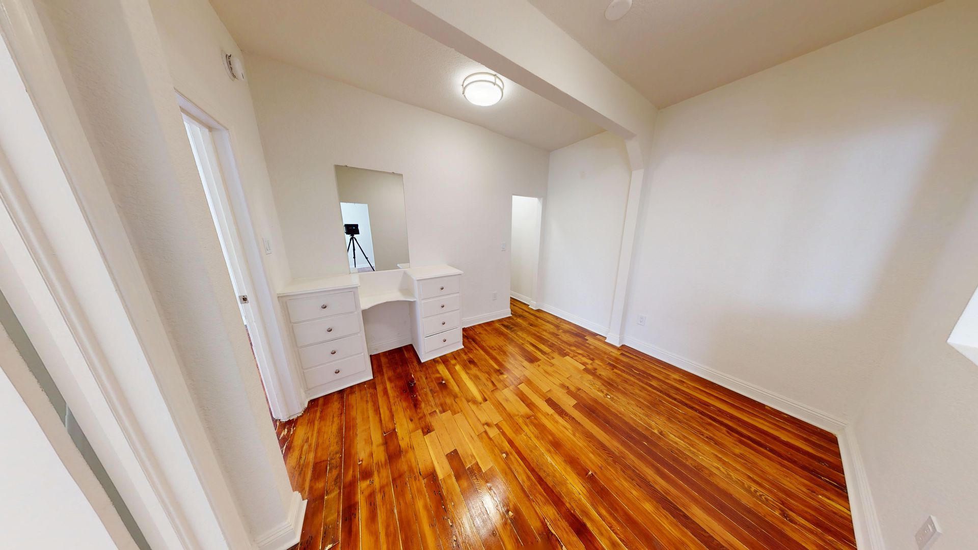 Empty room with wooden floor, white walls and built-in vanity with mirror.