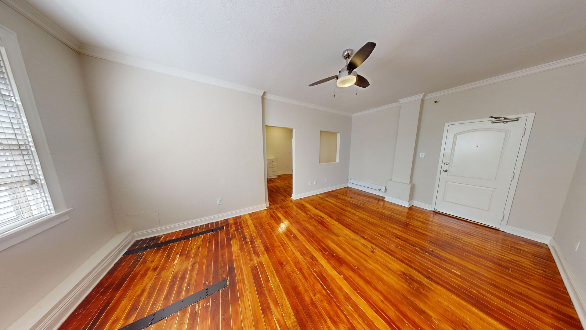 Empty room with wood floor, white walls and ceiling.  A door, window and hallway are visible.
