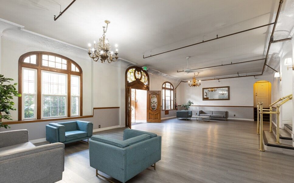 Spacious room with windows, seating, chandeliers, and open doorway; neutral color palette.