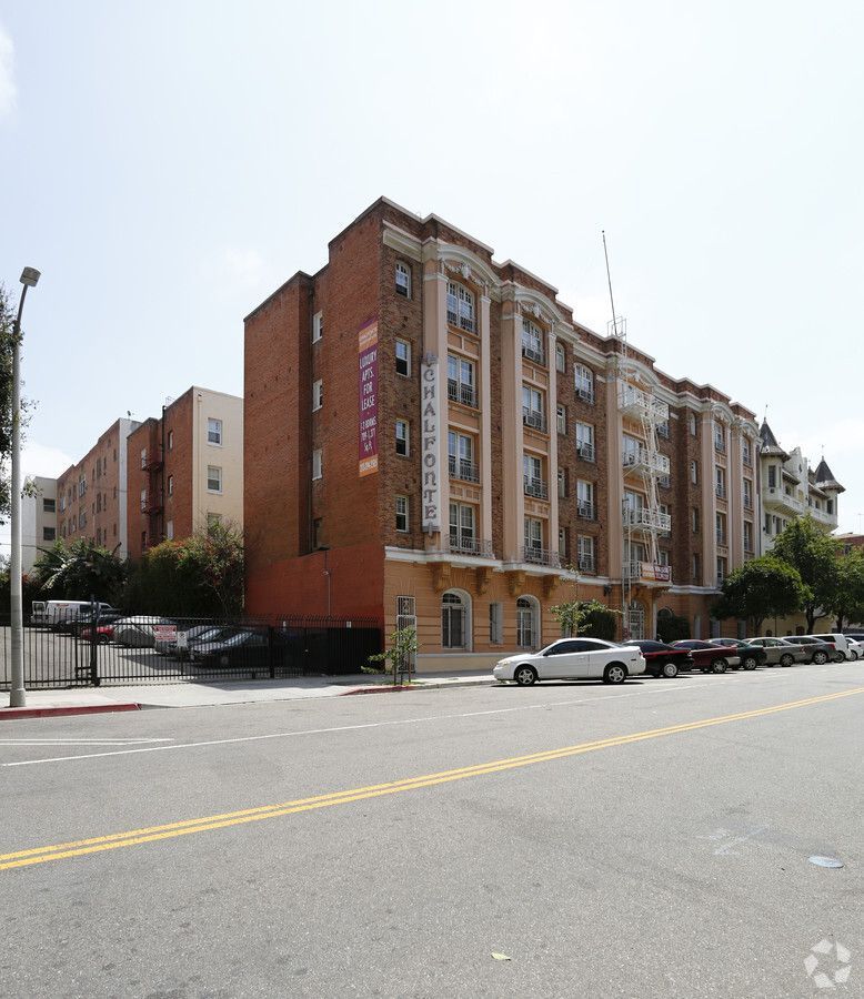 Multi-story brick apartment building on a city street, with cars parked along the curb.