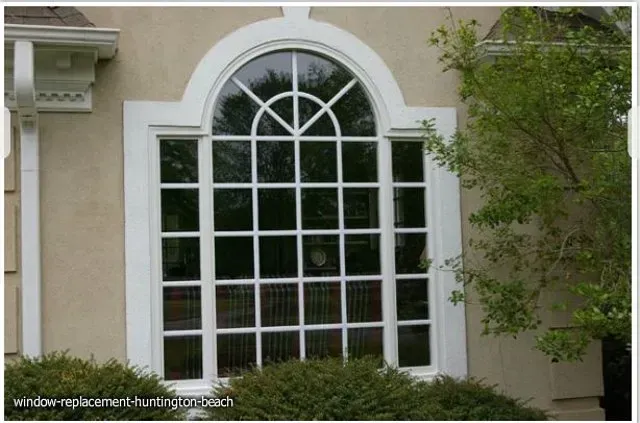 Large arched window with white frame on a beige building exterior, next to a tree.