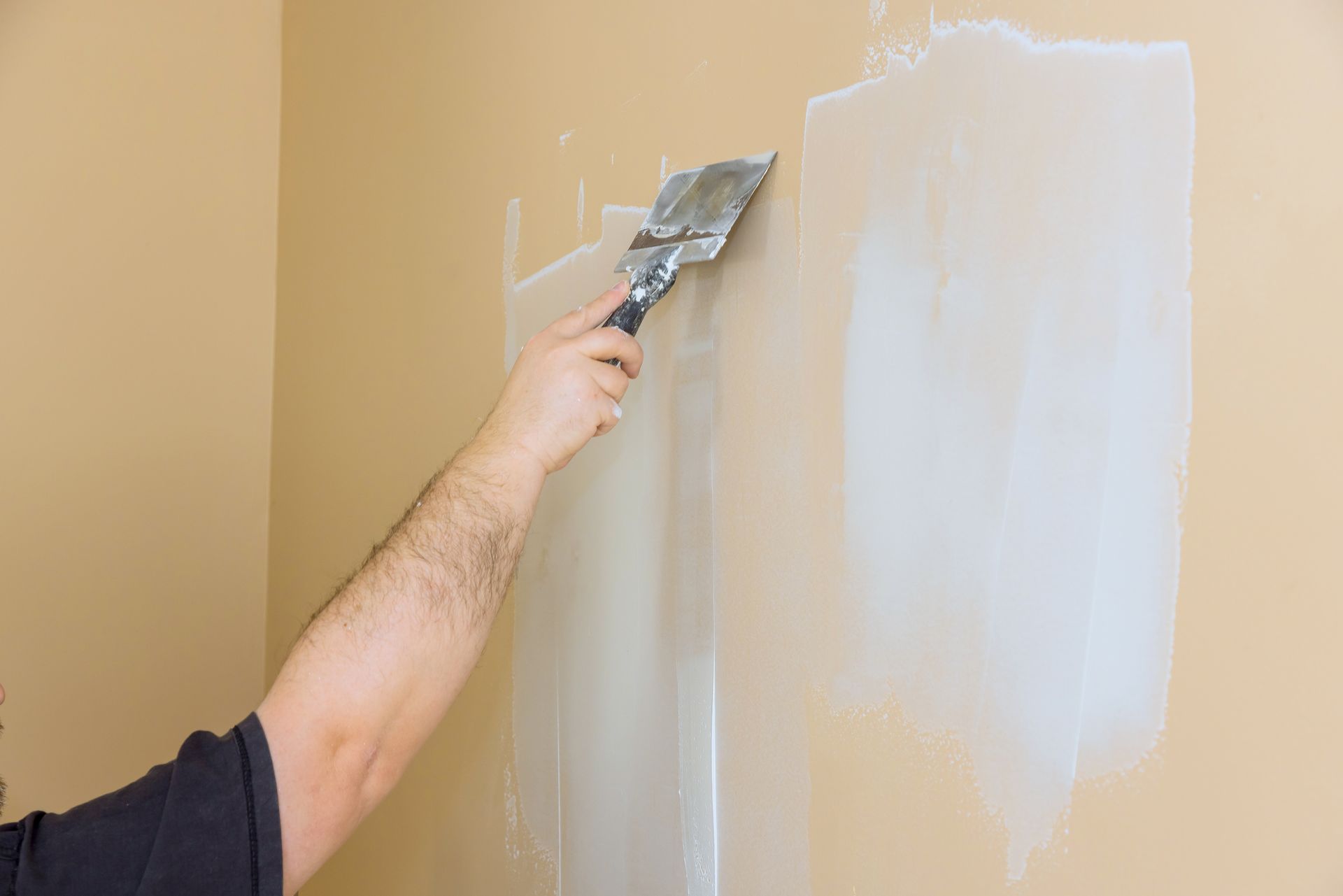 Person using a putty knife to apply drywall compound to a beige wall.