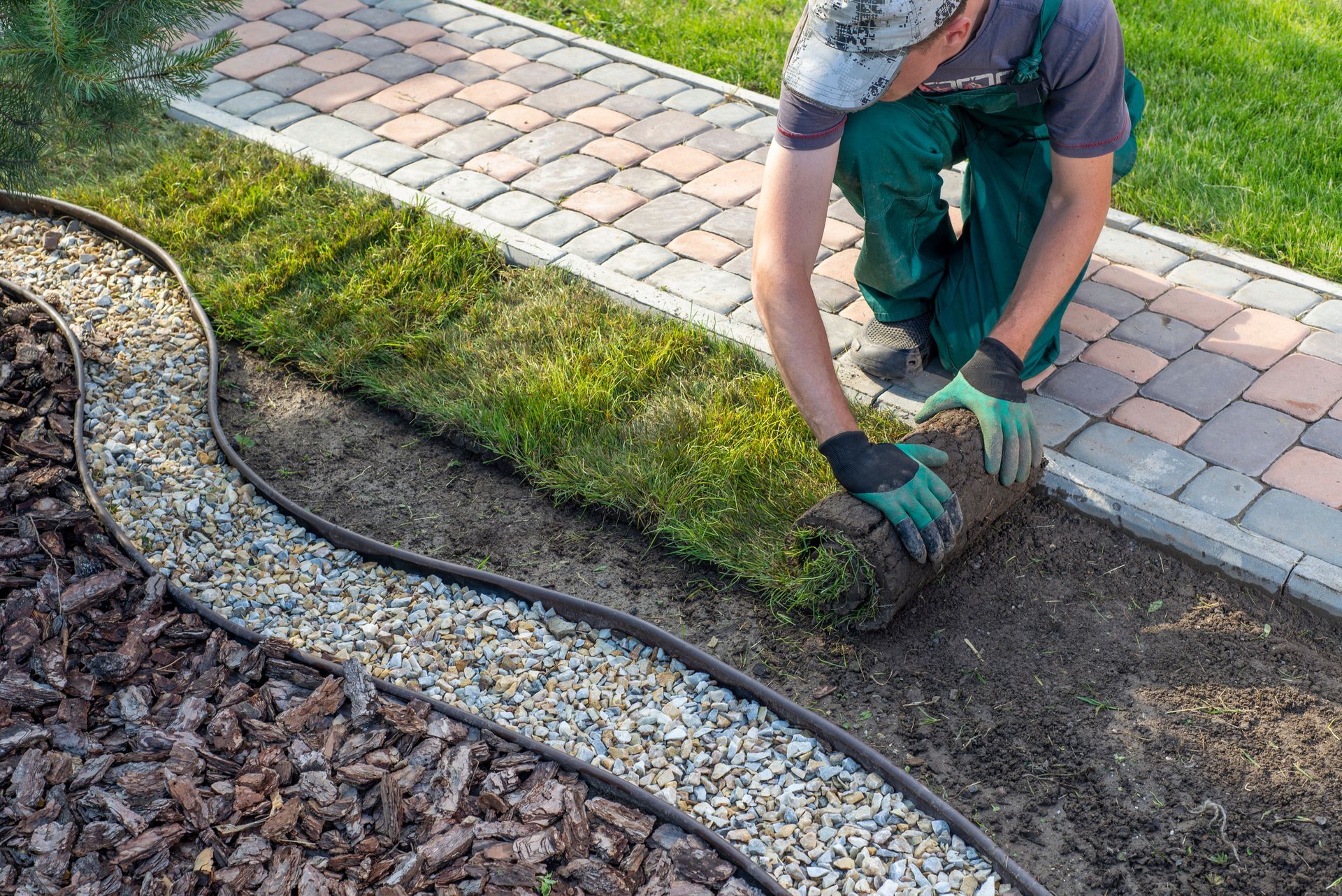 Man rolls out sod near a walkway, a rock bed, and lawn.