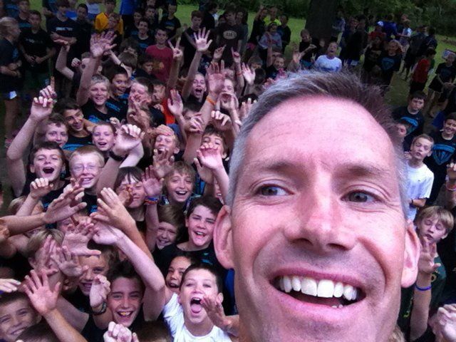 A man is taking a selfie in front of a crowd of children