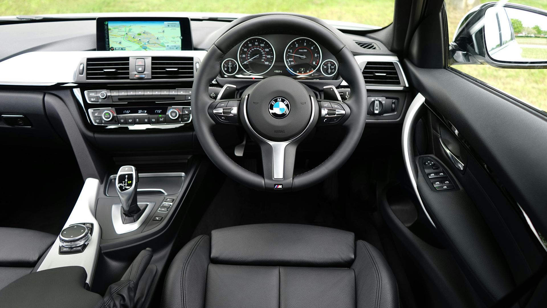 Interior view of a BMW car: dashboard, steering wheel, navigation screen, and black leather seats.