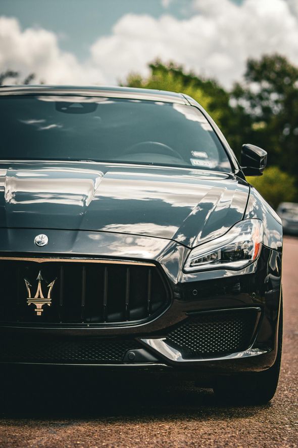 Black Maserati sedan parked, featuring gold Trident emblem on the front grille; outdoors on a sunny day.