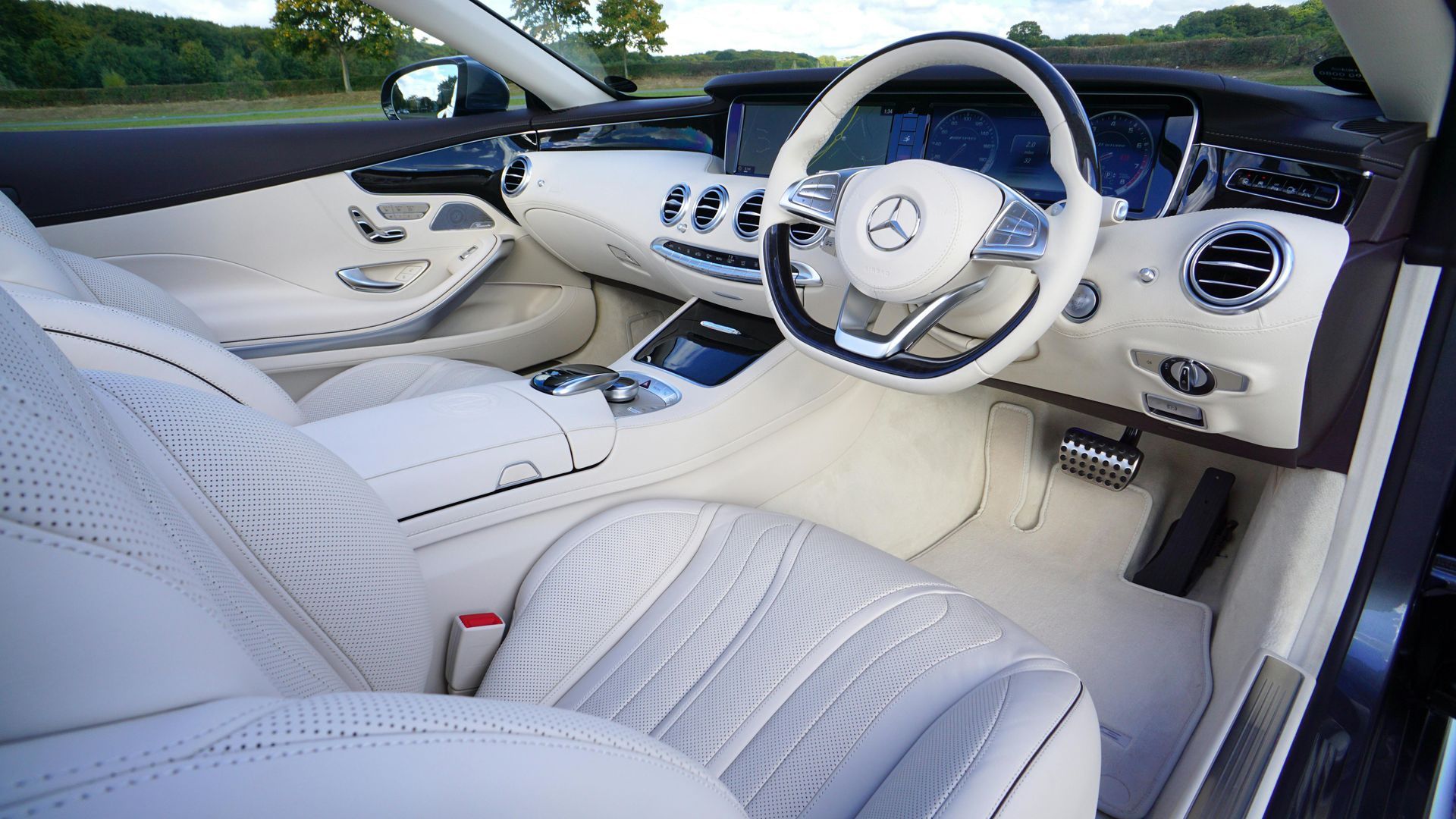 Cream-colored interior of a Mercedes convertible with white leather seats and steering wheel; dark brown trim.