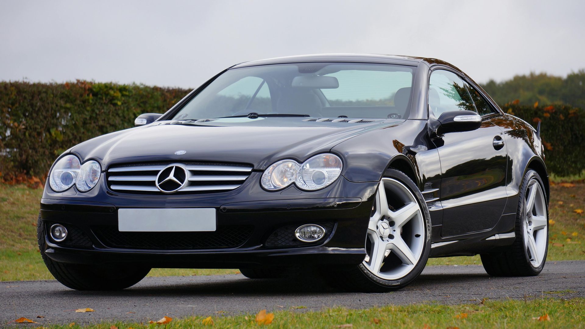 Black Mercedes SL convertible parked on a road, front view, overcast day.