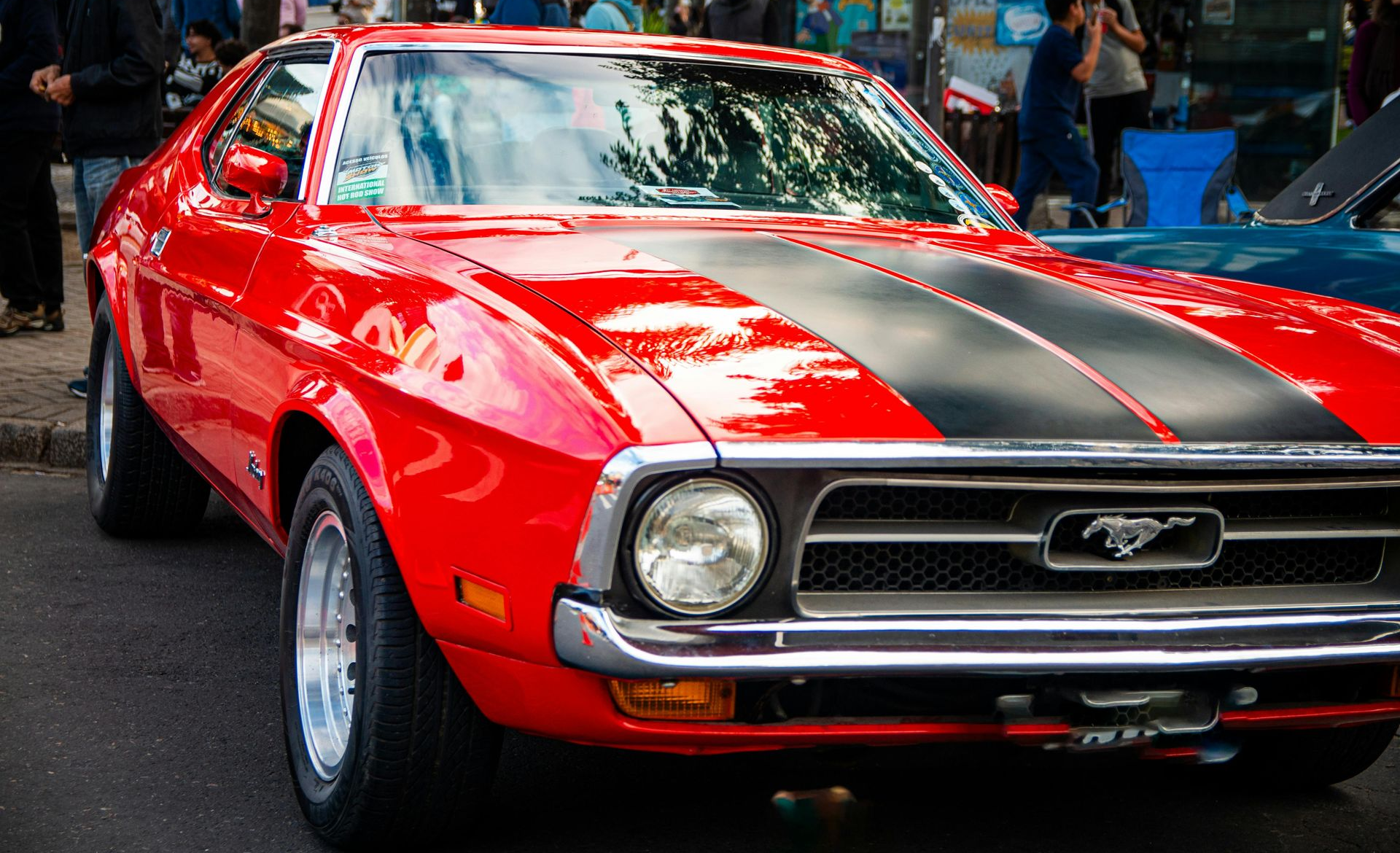 Red classic Mustang with black racing stripes, parked on a street.