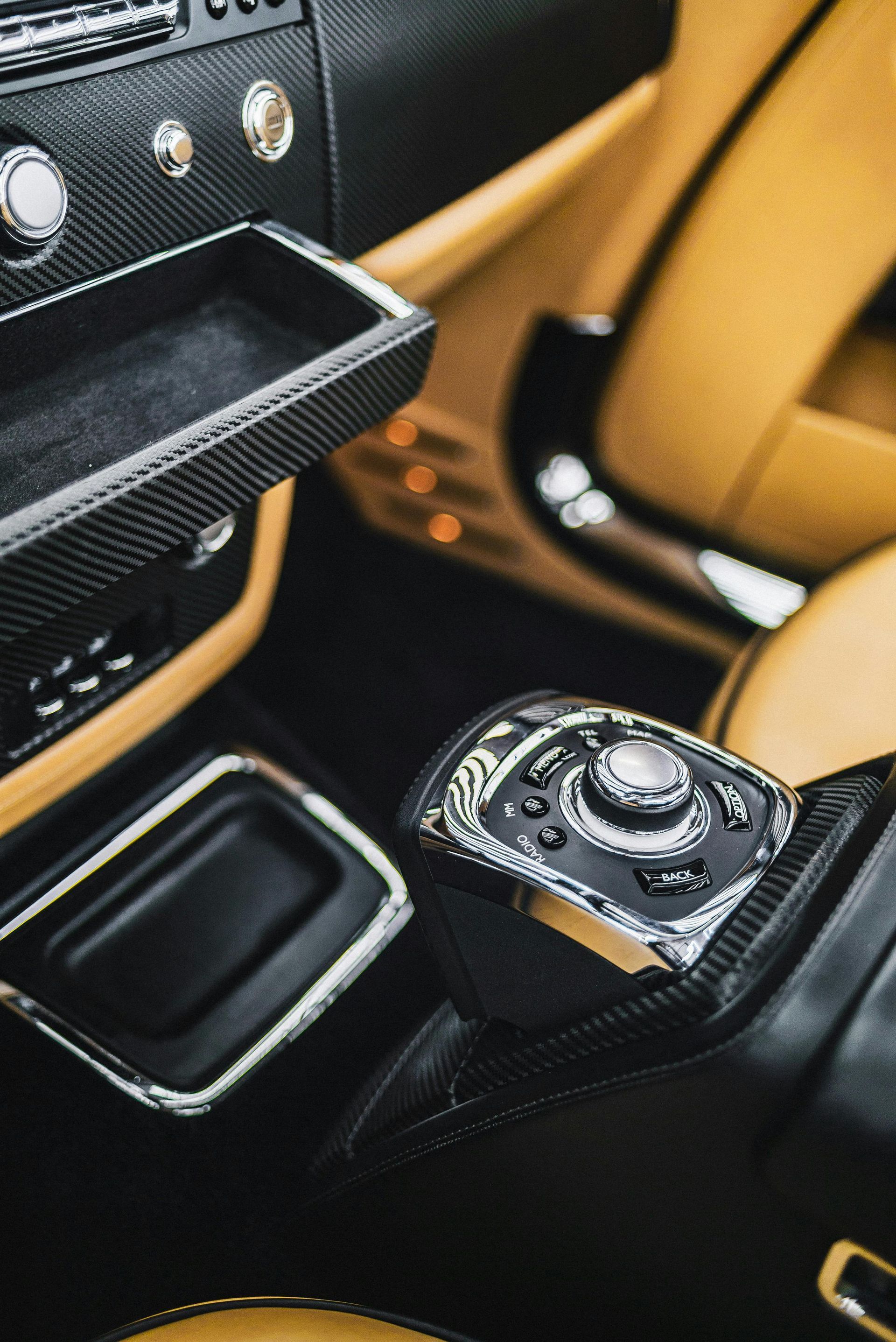 Close-up of a luxury car interior: leather seats, carbon fiber trim, metallic controls, and tan and black accents.