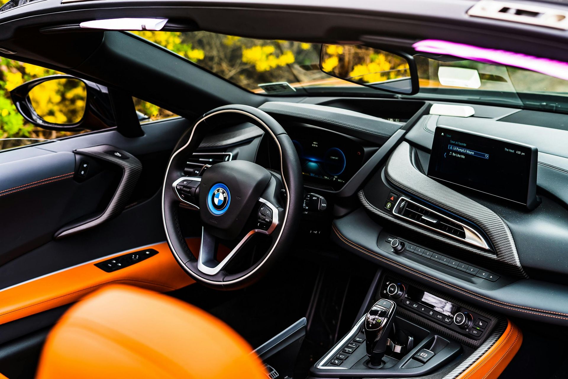 Interior of a luxury BMW i8 convertible, featuring black dashboard, orange accents, and a steering wheel.