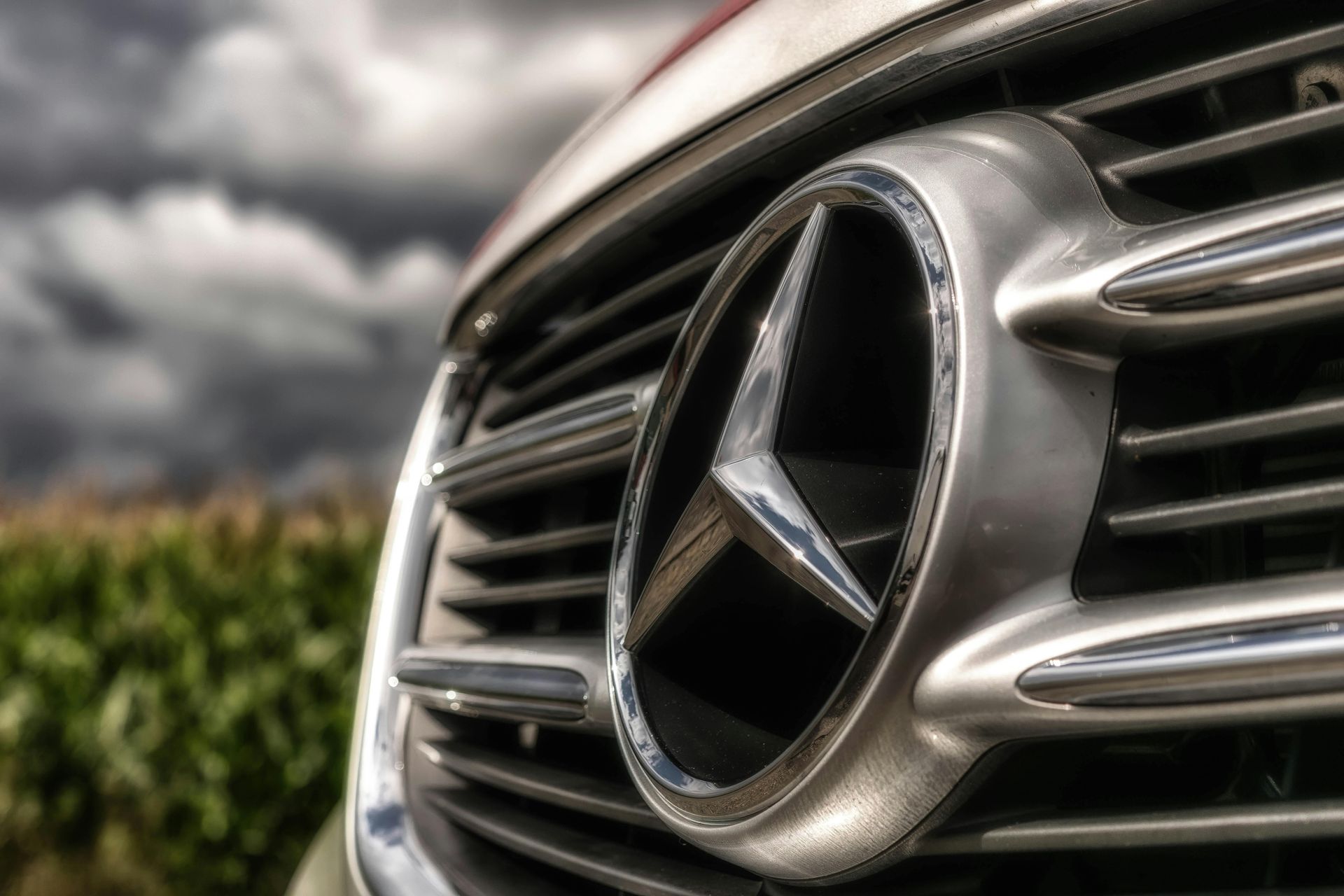Mercedes-Benz emblem on a silver grille with a cloudy sky background.