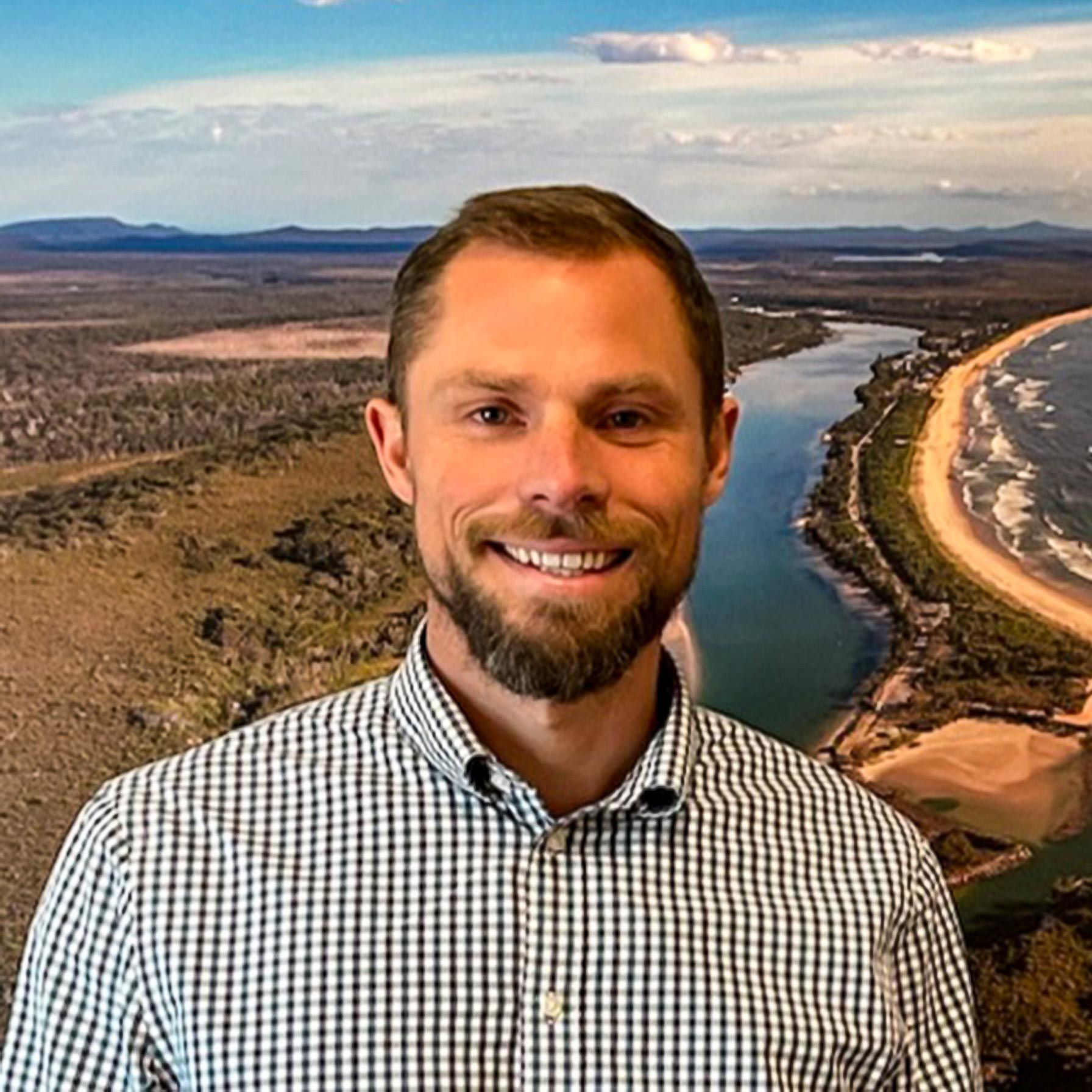Sam Gill - Chiropractor Bust shot of smiling man standing in front of scenic photo