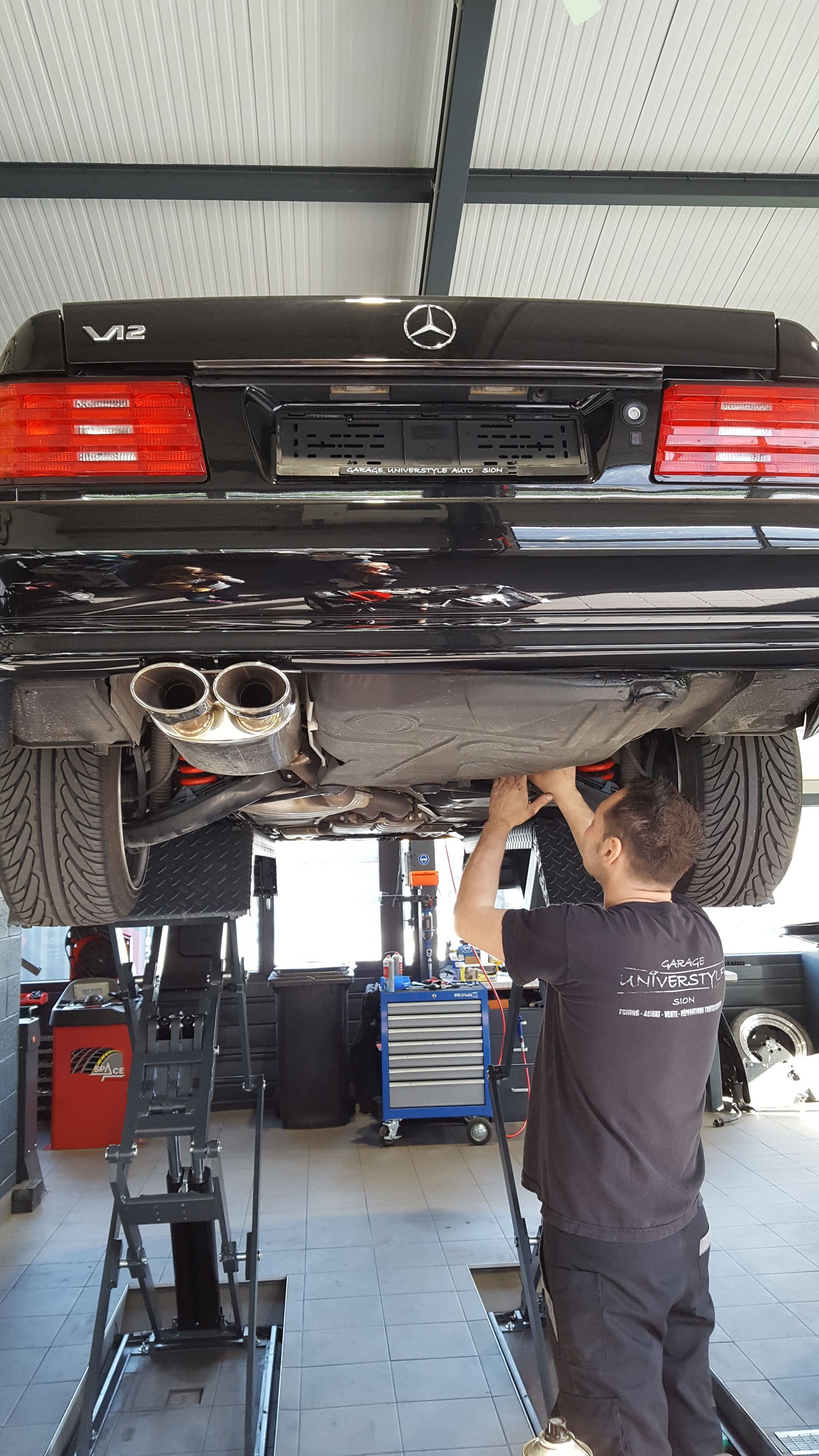 Un homme travaille sur le dessous d'une voiture dans un garage.