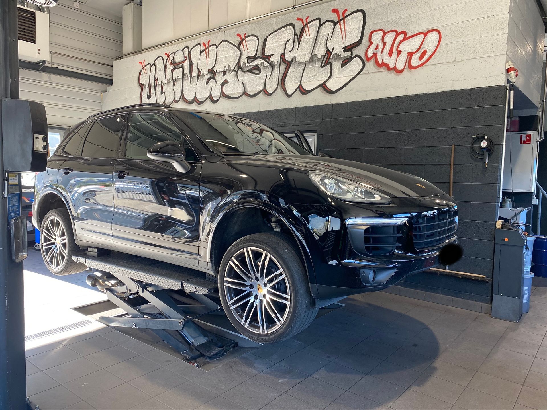 Une Porsche Cayenne noire est assise sur un ascenseur dans un garage.