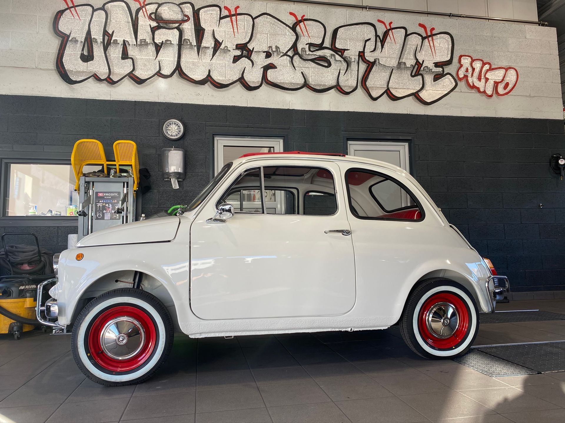 Une voiture blanche est garée devant un immeuble avec des graffitis dessus.