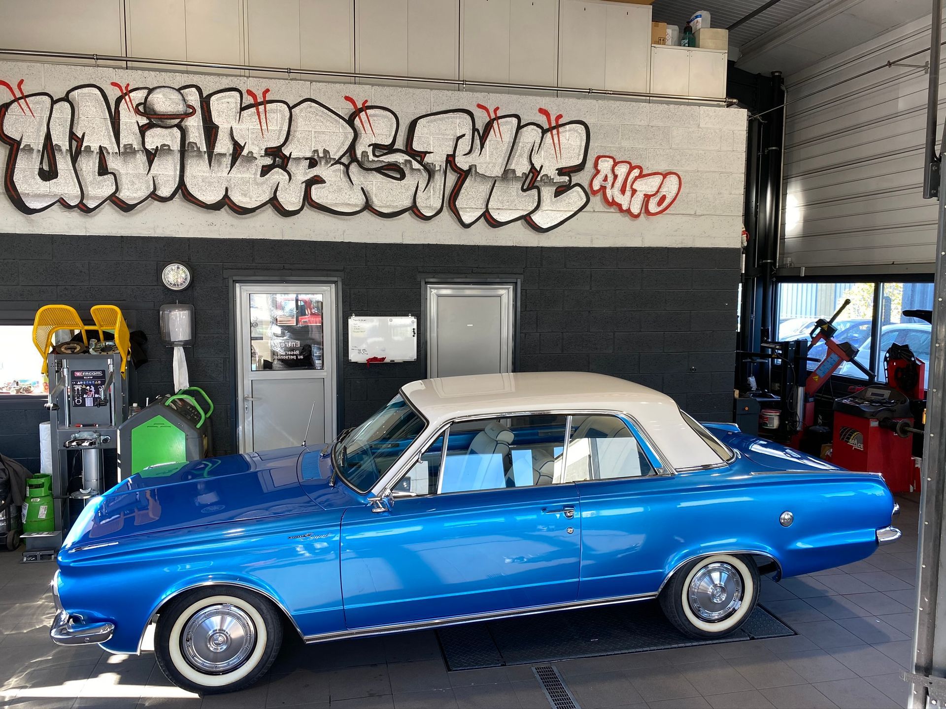 Une voiture bleue est garée devant un garage avec des graffitis sur le mur.