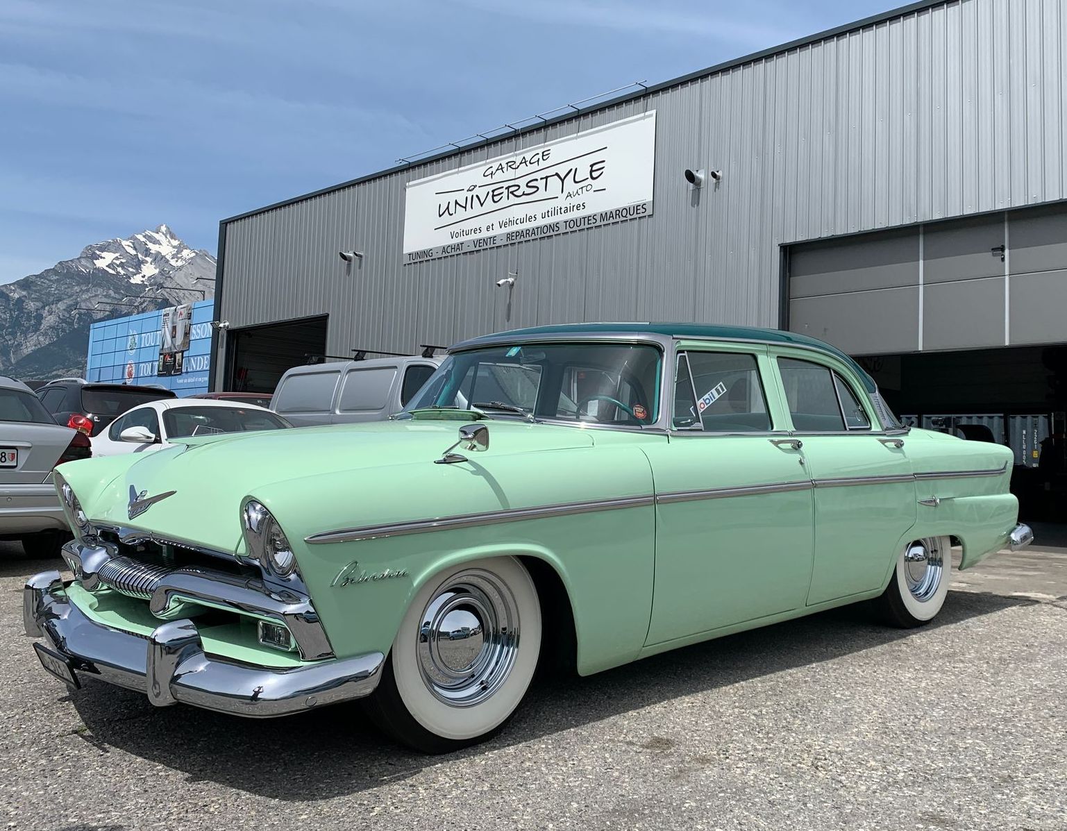 Une voiture verte est garée devant un immeuble.