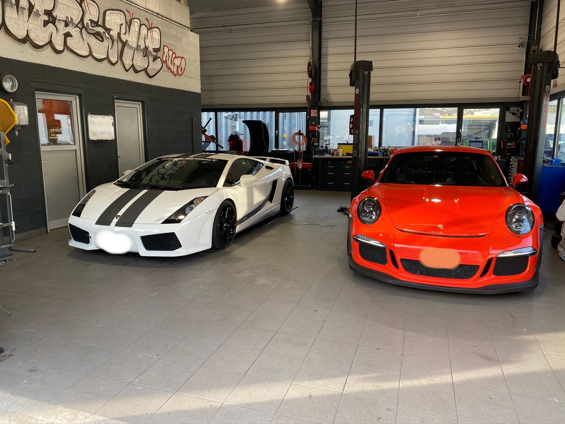 Une Lamborghini blanche et une Porsche orange sont garées dans un garage.