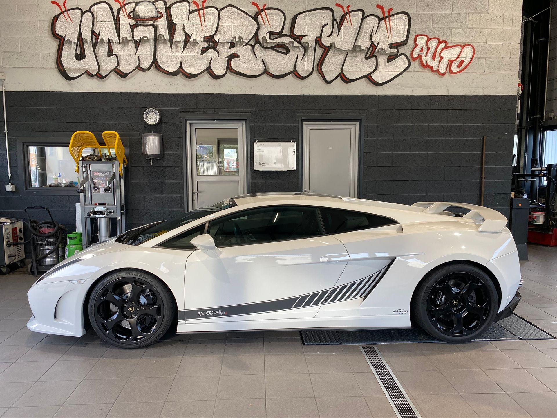 Une voiture de sport blanche est garée devant un mur avec des graffitis dessus.