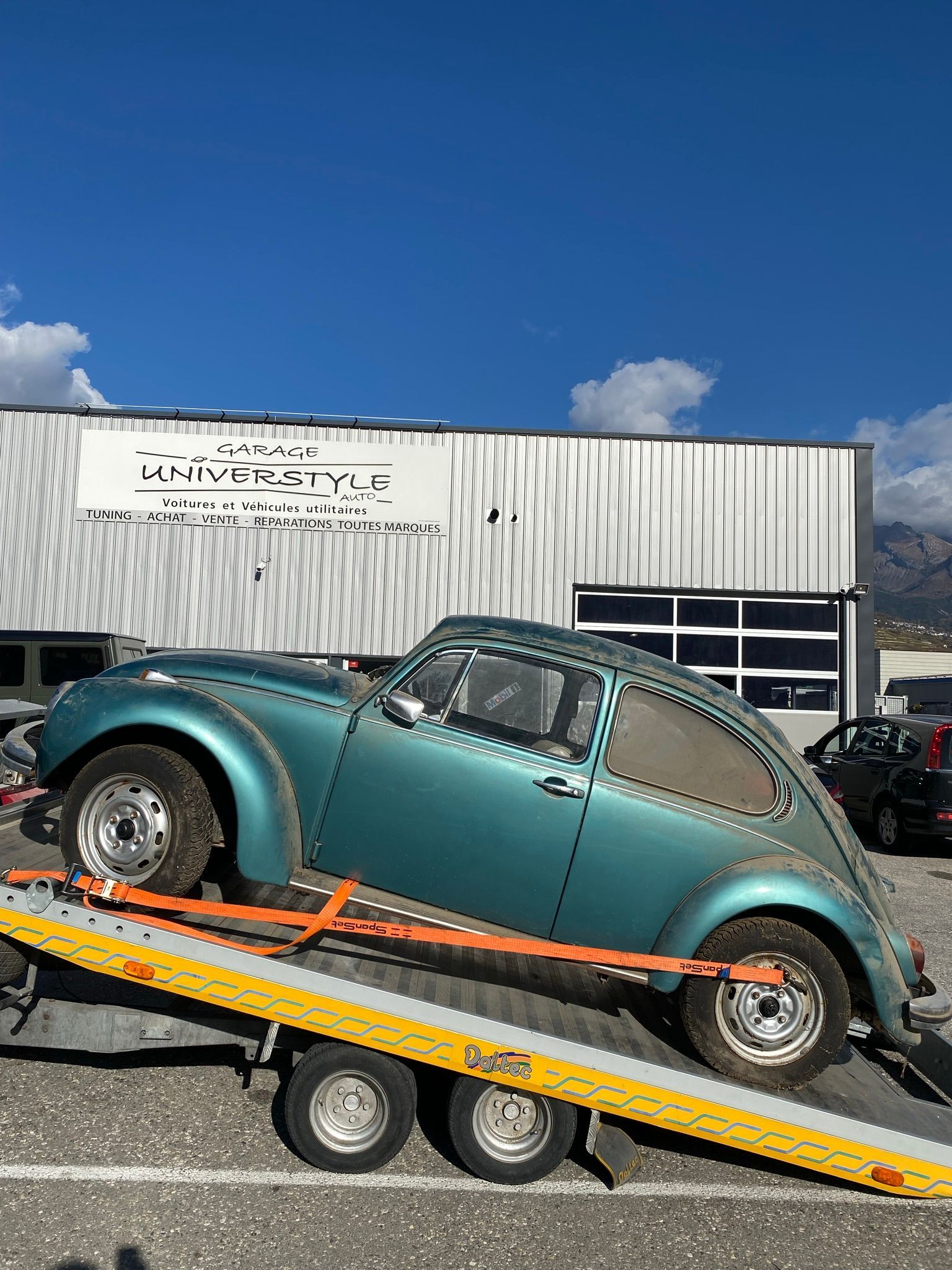 Une voiture verte est remorquée par une dépanneuse.