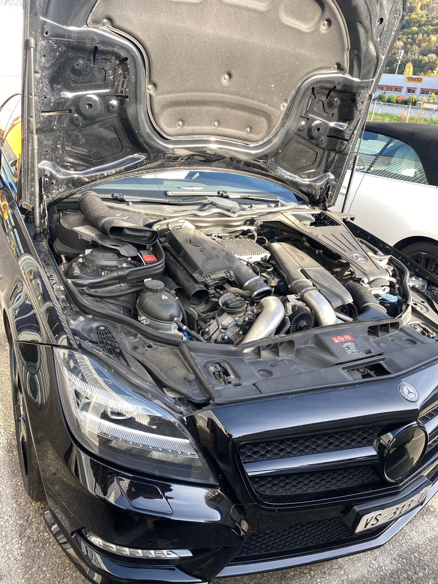 Le capot d'une voiture noire est ouvert et le moteur est visible.