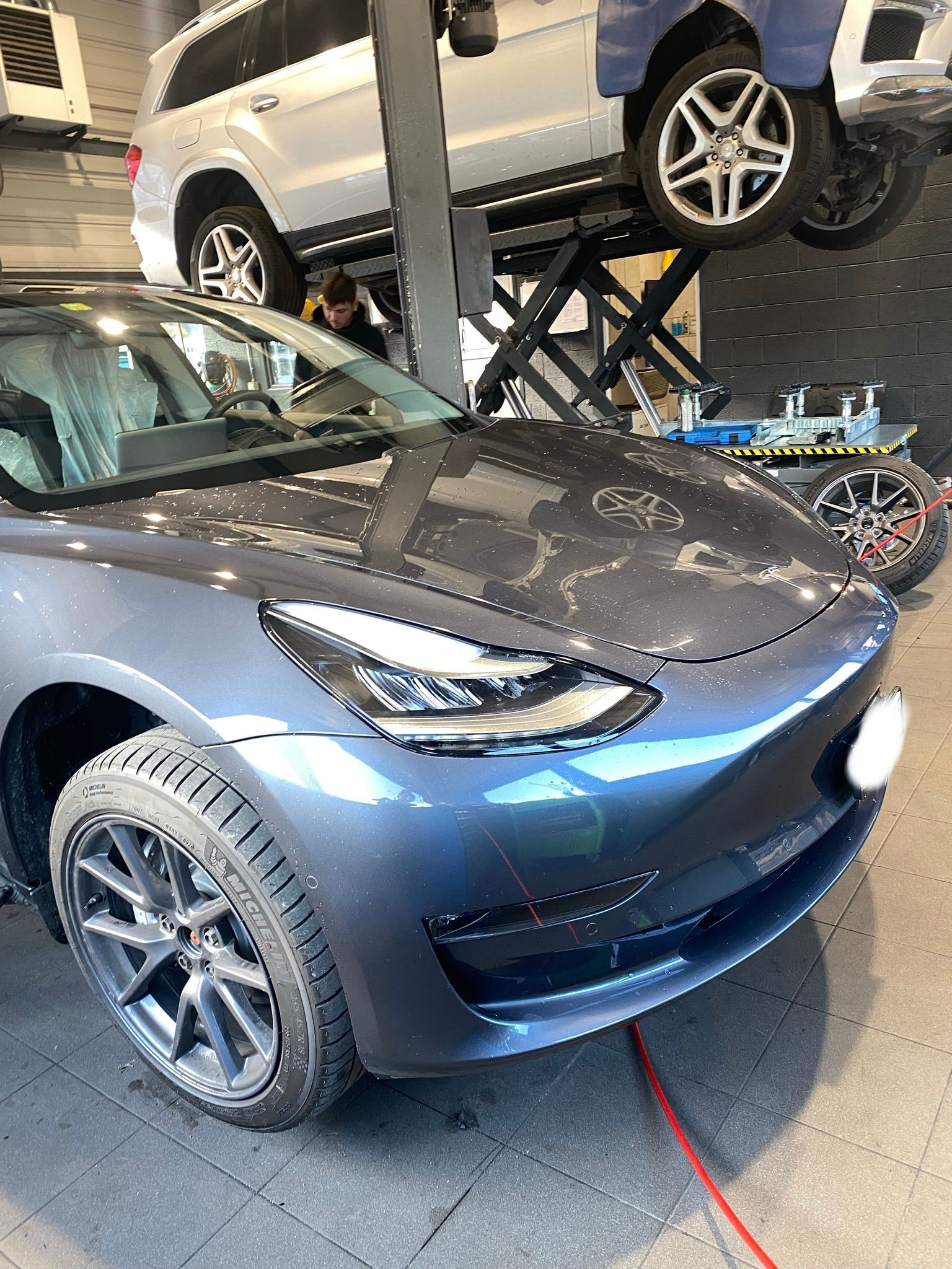 Une Tesla Model 3 est posée sur un ascenseur dans un garage.