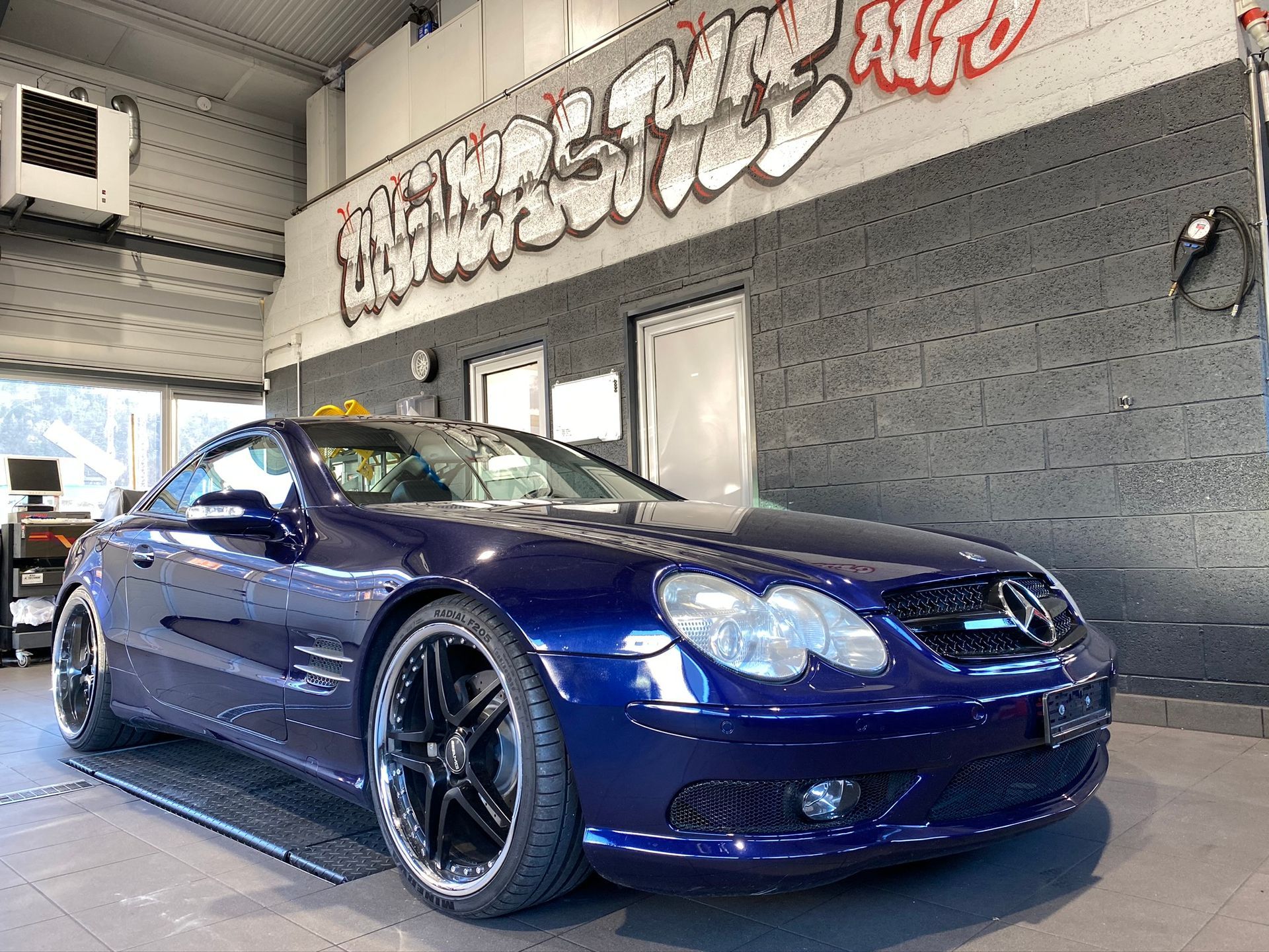 Une voiture de sport bleue est garée dans un garage avec des graffitis sur le mur.