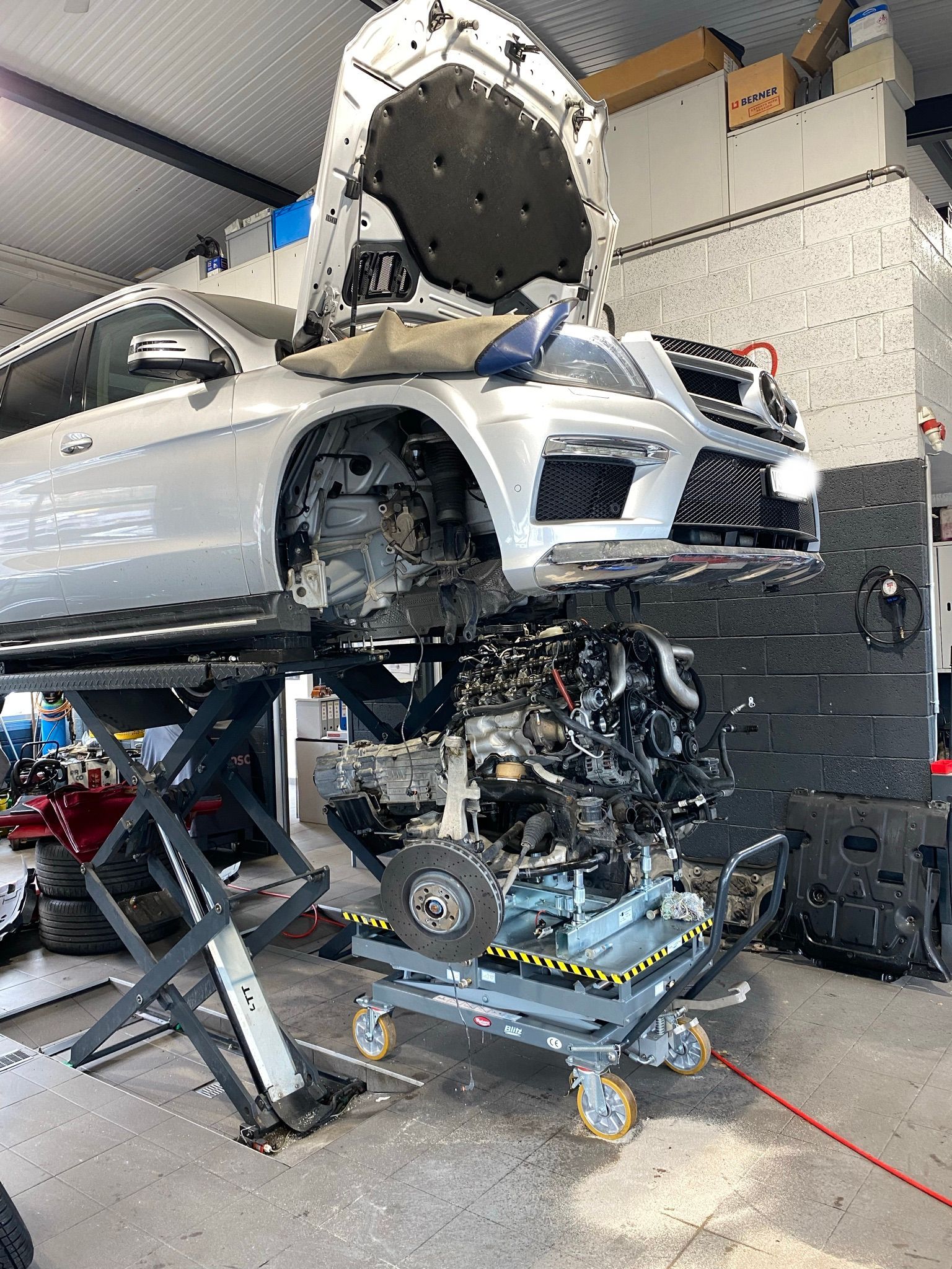 Une voiture est posée sur un ascenseur dans un garage avec le capot relevé.