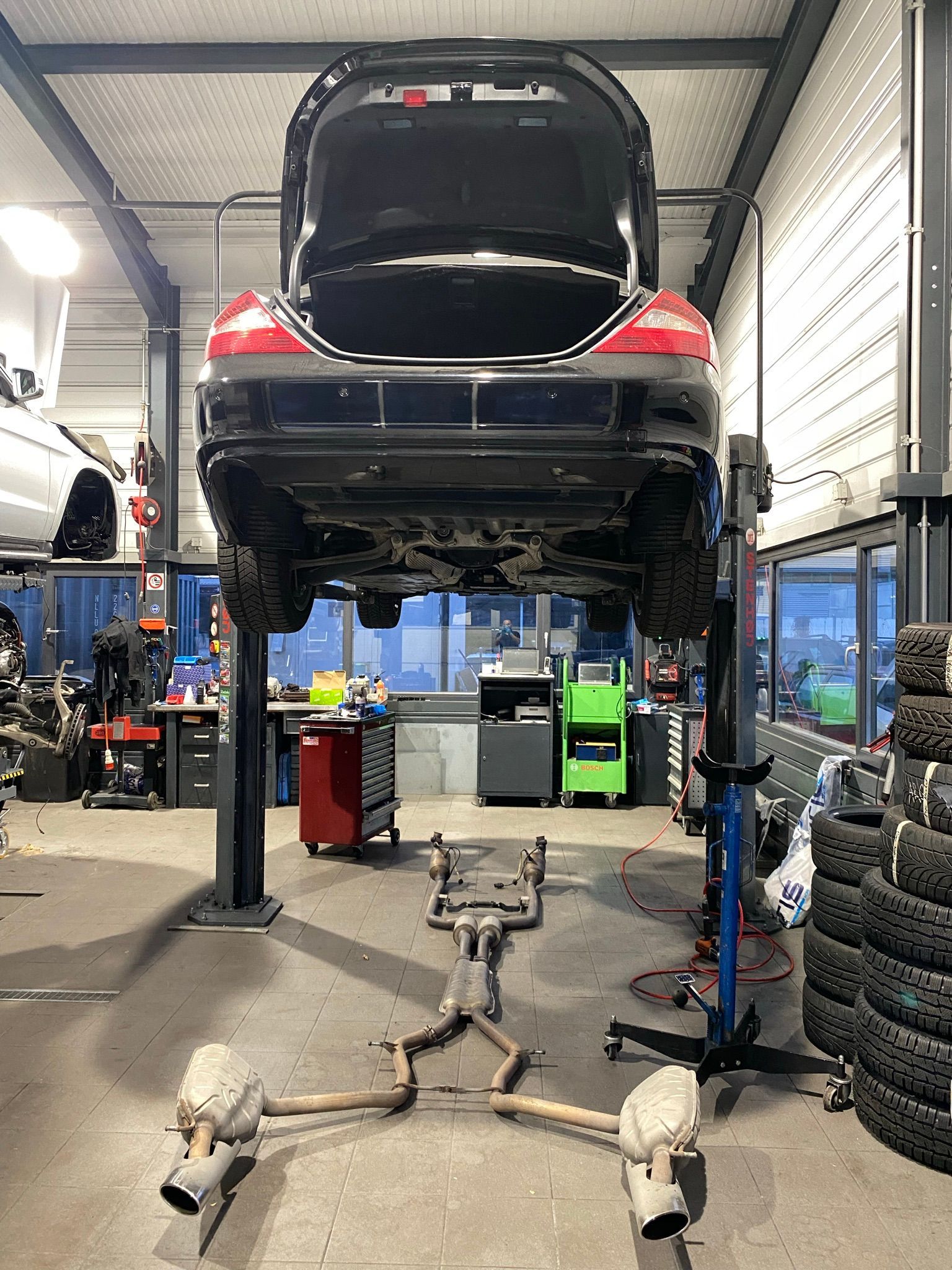 Une voiture est posée sur un ascenseur dans un garage avec le coffre ouvert.