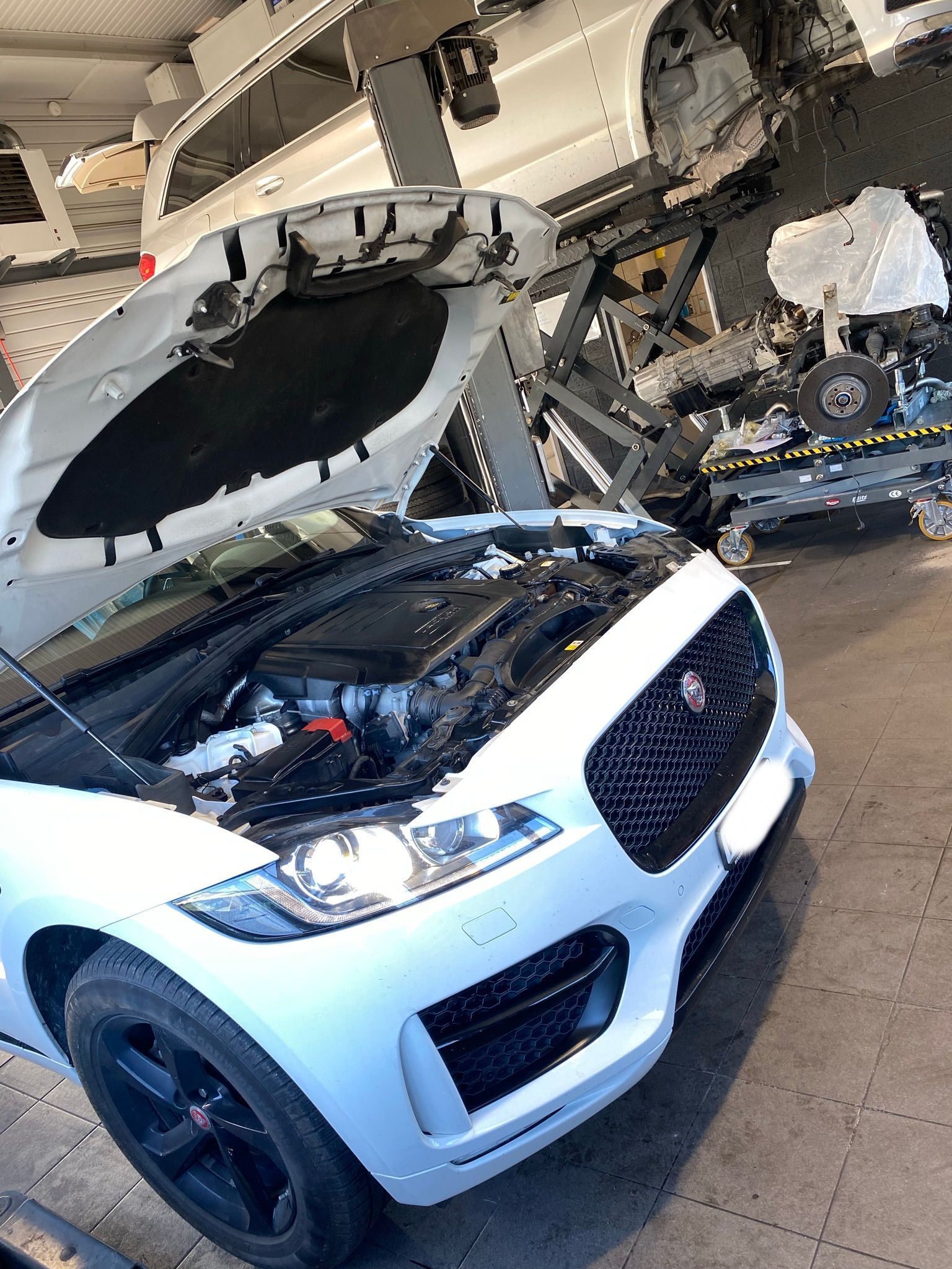 Une voiture blanche avec le capot ouvert est assise dans un garage.