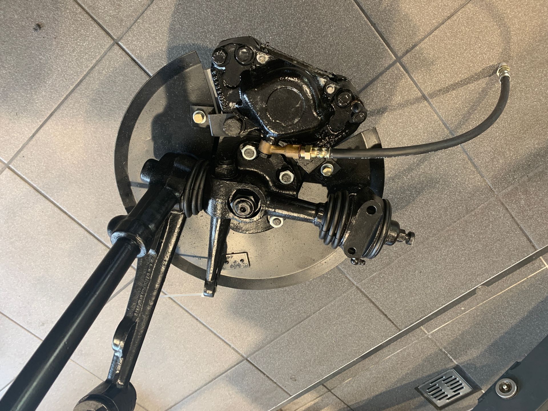 Un étrier de frein noir repose sur un sol carrelé.