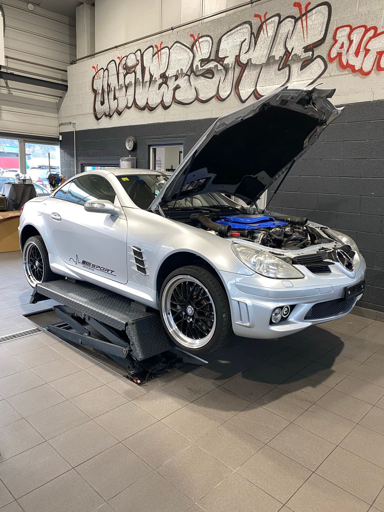 Une voiture de sport argentée avec le capot relevé est garée dans un garage.