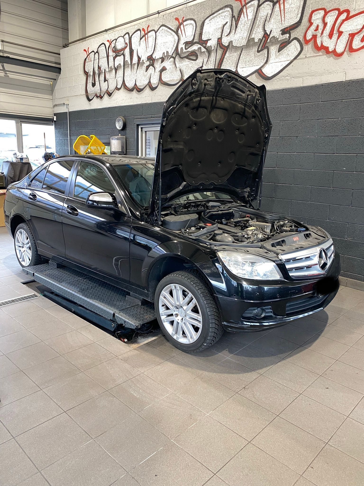 Une voiture noire avec le capot relevé est assise sur un ascenseur dans un garage.