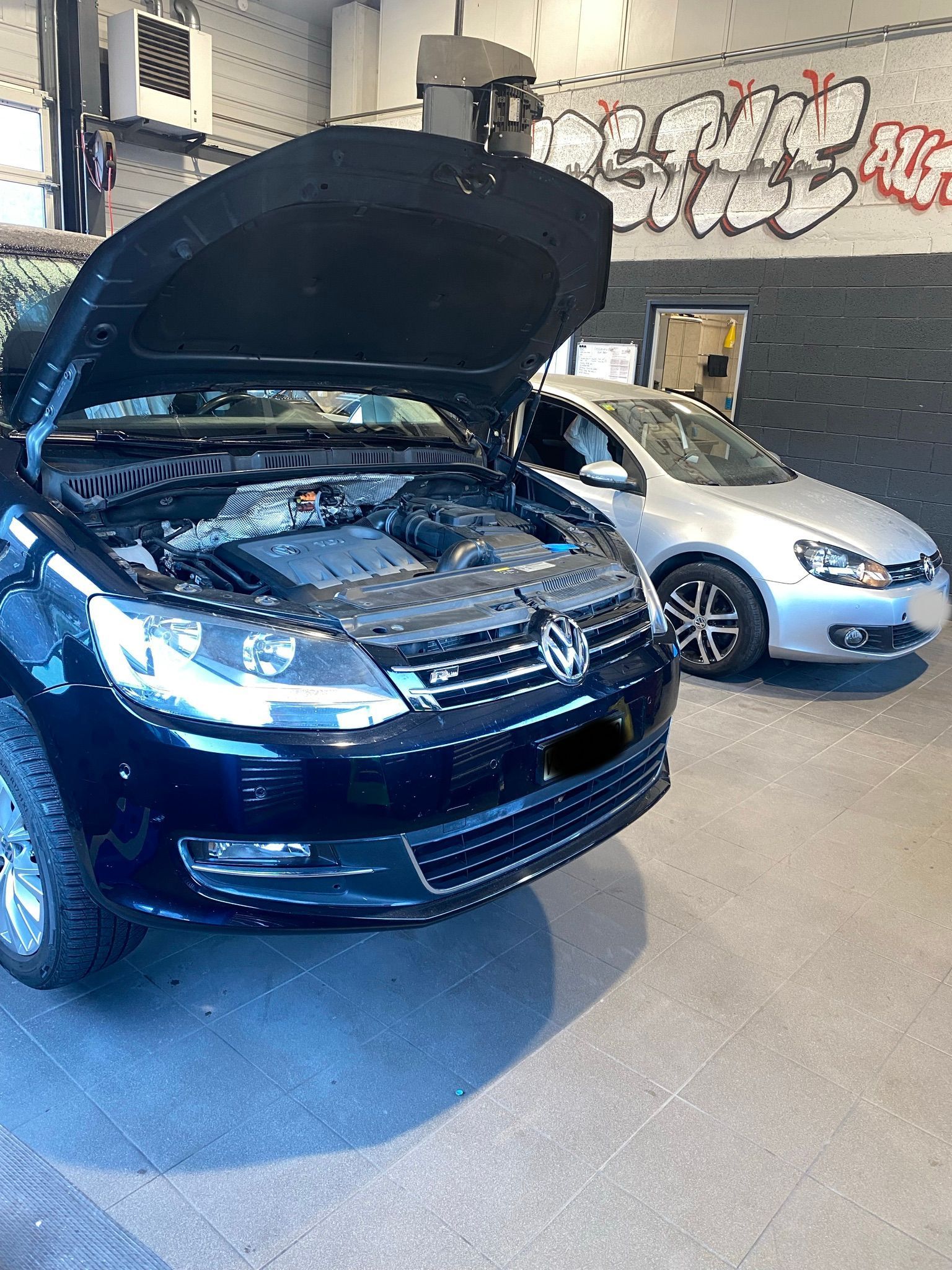 Deux voitures sont garées dans un garage avec le capot ouvert.